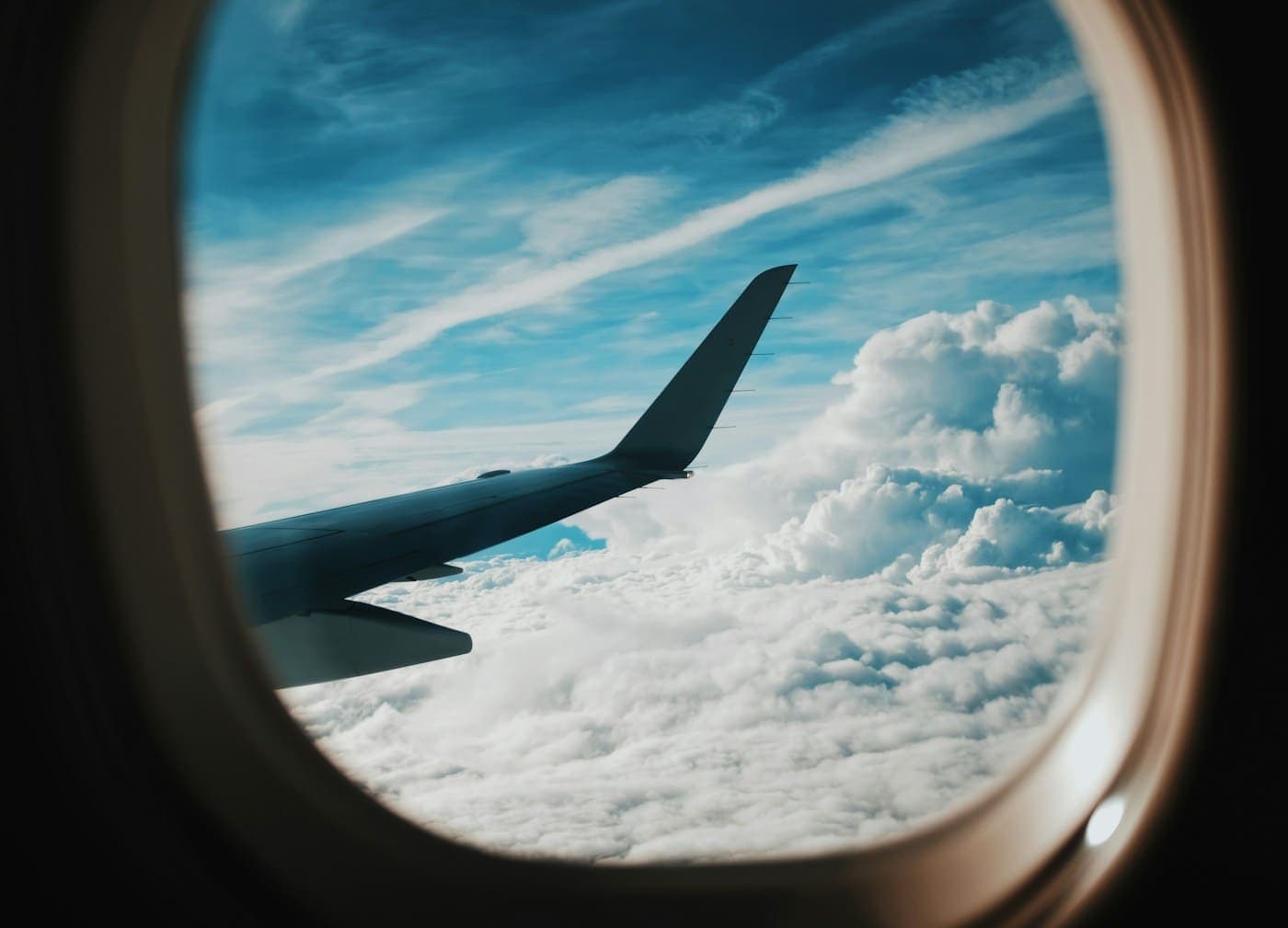 The wing of an aeroplane seen through a cabin window, above a thick layer of cloud.