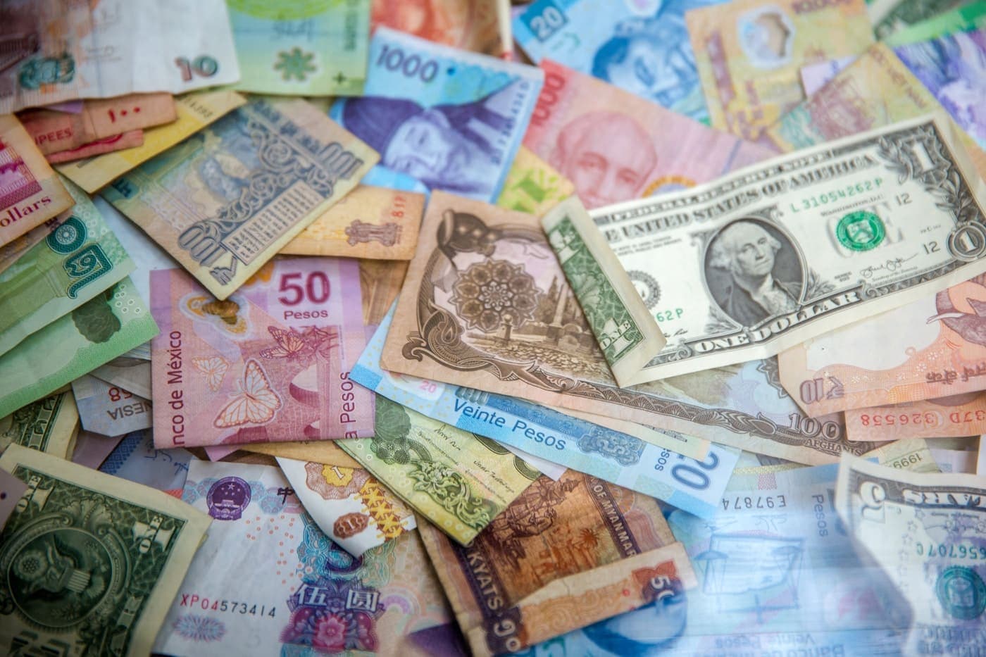 Banknotes from many different countries spread out and overlapping on a flat surface.