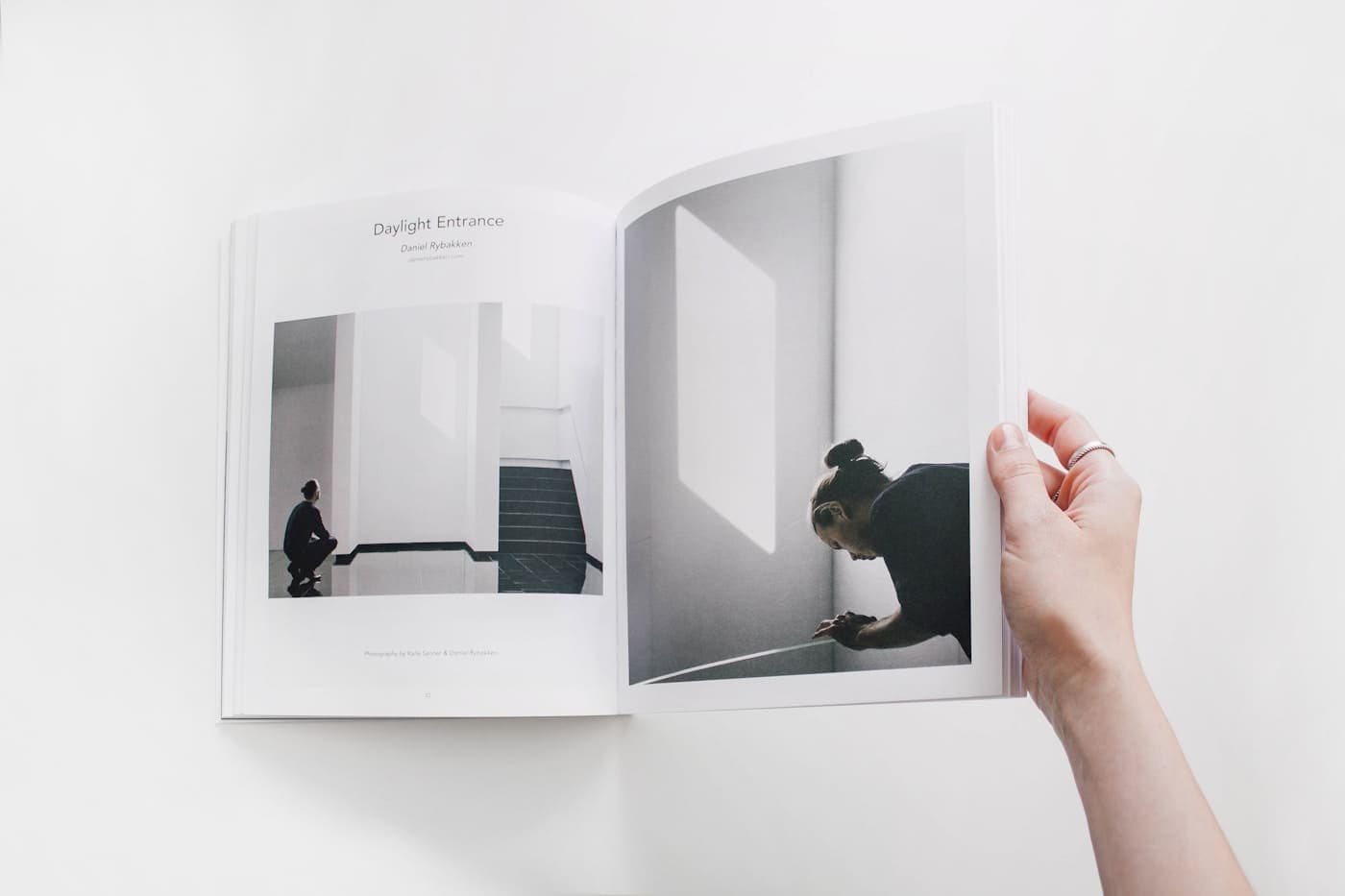 A hand holding open a photo book to a two-page spread of black-and-white photographs.