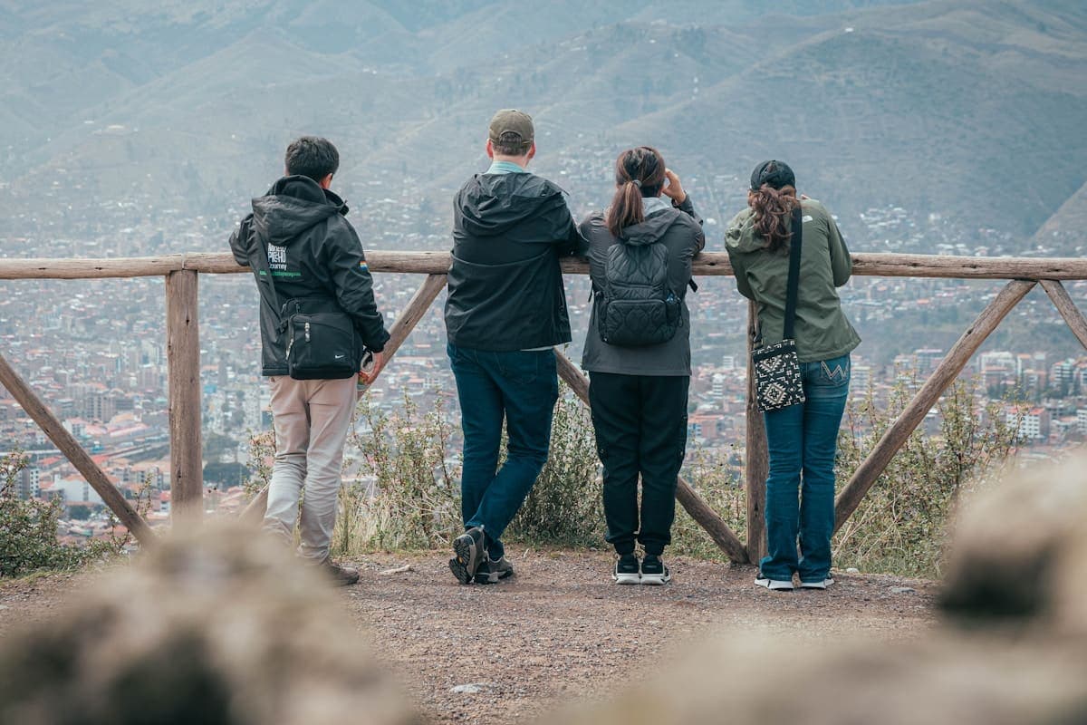 Four friends in jackets and backpacks standing at a railing, looking out over a valley together.