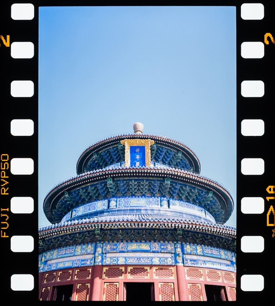 A tiered blue-and-gold temple roof against a clear sky, framed by the sprocket holes of a 35mm film strip.